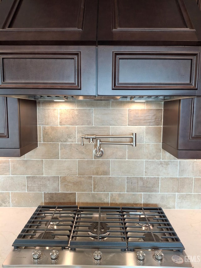 kitchen featuring stainless steel gas stovetop, dark brown cabinets, and light stone counters