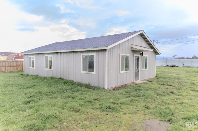 view of home's exterior featuring a shingled roof, fence, and a lawn