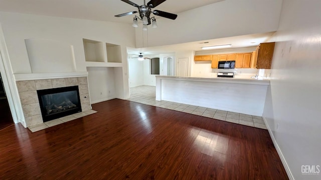 unfurnished living room with a tiled fireplace, ceiling fan, light hardwood / wood-style floors, and lofted ceiling