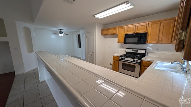 kitchen featuring ceiling fan, sink, stainless steel range with gas cooktop, tile patterned floors, and tile countertops