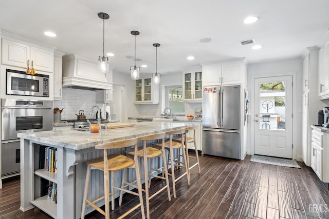 kitchen featuring white cabinetry, stainless steel appliances, light stone counters, and a center island with sink