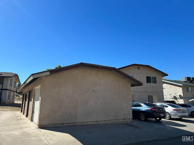 view of side of property featuring uncovered parking, central air condition unit, and stucco siding