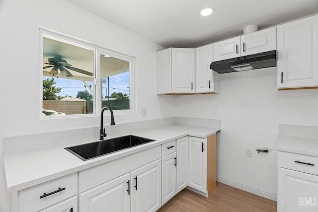 1317 Canyon Ct, Bakersfield, CA 93307 - kitchen with under cabinet range hood, a sink, light wood-type flooring, white cabinetry, and light countertops