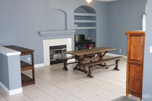 dining room featuring built in shelves, light tile patterned flooring, baseboards, and a tile fireplace