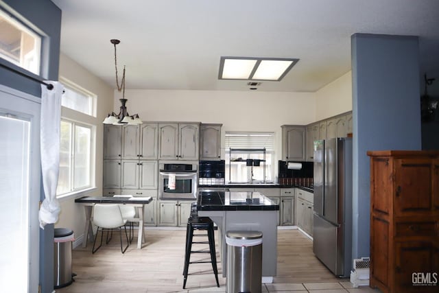 kitchen featuring a kitchen bar, light wood-style flooring, a center island, stainless steel appliances, and hanging light fixtures