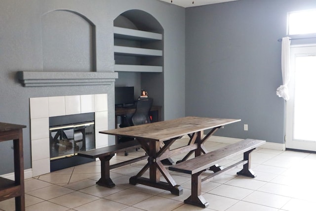 dining space with light tile patterned floors, built in shelves, a fireplace, and baseboards