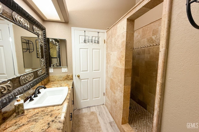 full bathroom featuring wood finished floors, a skylight, tiled shower, vanity, and a textured wall