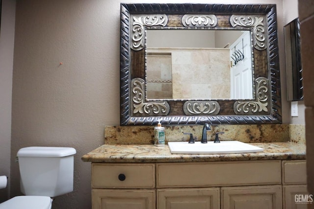 half bathroom with toilet, vanity, and a textured wall