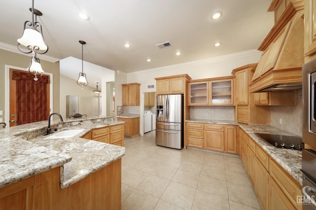 kitchen featuring black electric stovetop, sink, stainless steel fridge, decorative light fixtures, and light stone counters