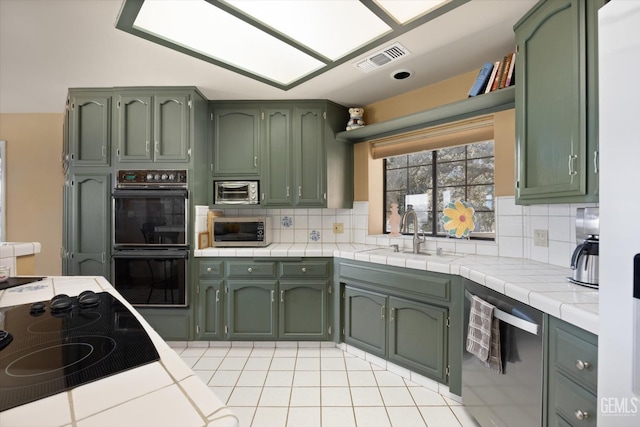 kitchen featuring decorative backsplash, sink, black appliances, tile countertops, and green cabinetry