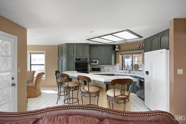 kitchen featuring a breakfast bar, green cabinets, white fridge with ice dispenser, black oven, and dishwashing machine