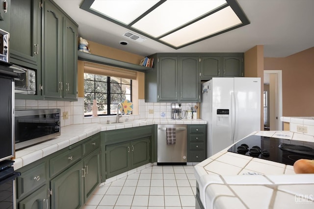 kitchen featuring tile counters, sink, stainless steel appliances, and green cabinetry