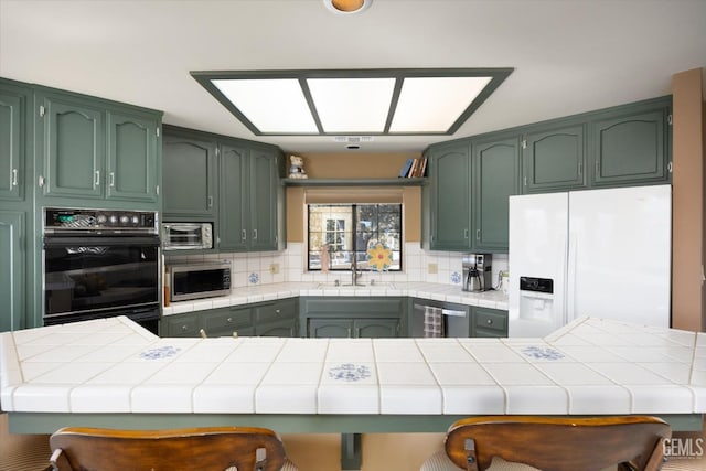 kitchen featuring a kitchen bar, stainless steel appliances, kitchen peninsula, and green cabinets