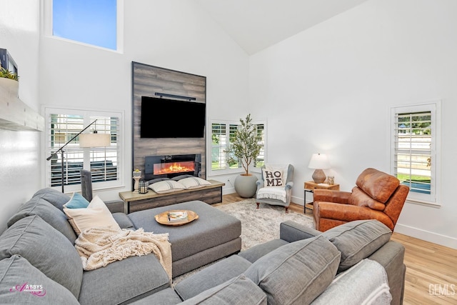 living room with a wealth of natural light, a glass covered fireplace, wood finished floors, and high vaulted ceiling