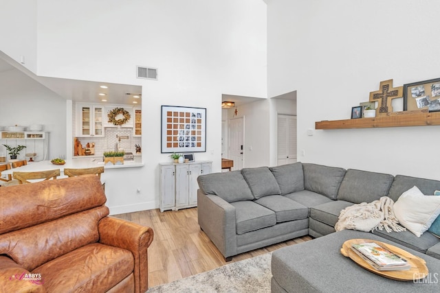 living room featuring recessed lighting, a high ceiling, visible vents, baseboards, and light wood-style flooring