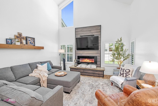 living area with a glass covered fireplace, wood finished floors, a towering ceiling, and baseboards