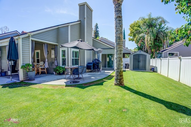back of property featuring a patio area, a shed, a lawn, a fenced backyard, and an outbuilding