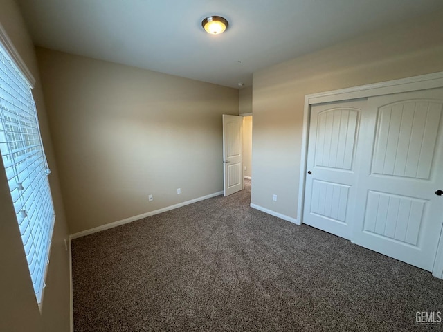unfurnished bedroom featuring dark carpet, baseboards, and a closet