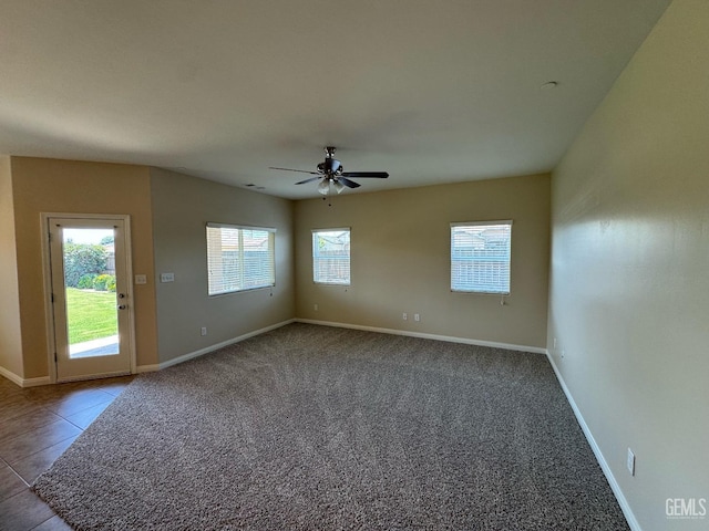 carpeted empty room featuring baseboards, a ceiling fan, and tile patterned floors