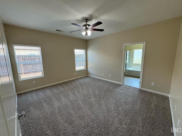 carpeted spare room featuring a ceiling fan, baseboards, visible vents, and a healthy amount of sunlight