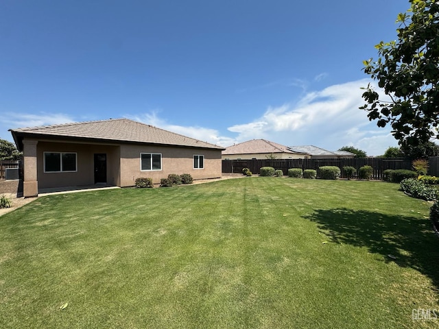 back of house featuring a lawn, a tiled roof, a fenced backyard, and stucco siding