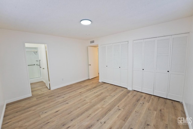 unfurnished bedroom with light wood finished floors, two closets, visible vents, and baseboards