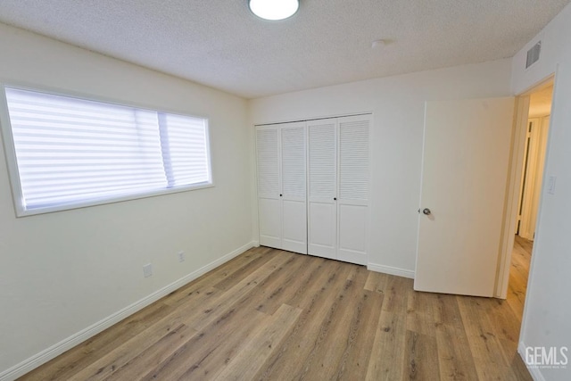 unfurnished bedroom featuring light wood finished floors, a textured ceiling, visible vents, and a closet