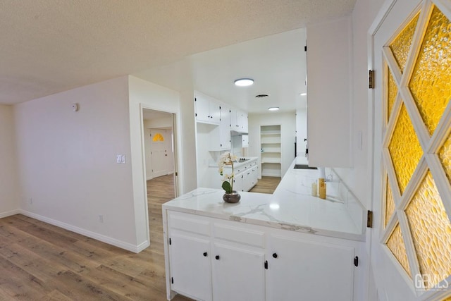 kitchen with light wood finished floors, baseboards, light stone counters, a peninsula, and white cabinetry