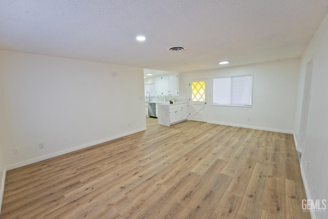 empty room featuring a textured ceiling, baseboards, visible vents, and light wood-style floors