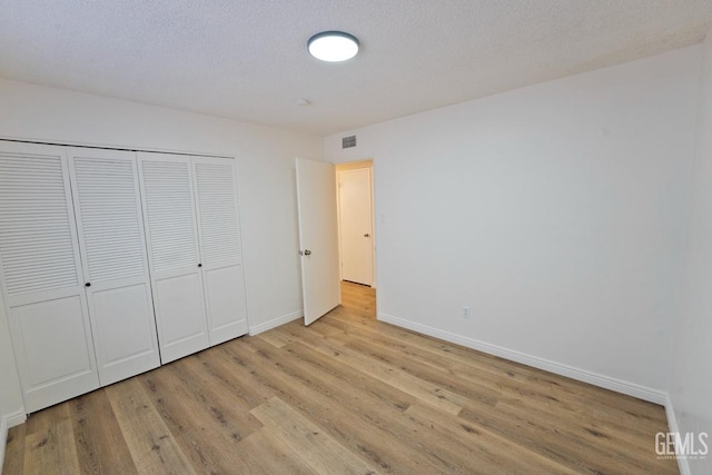 unfurnished bedroom with light wood-style floors, visible vents, a textured ceiling, and baseboards