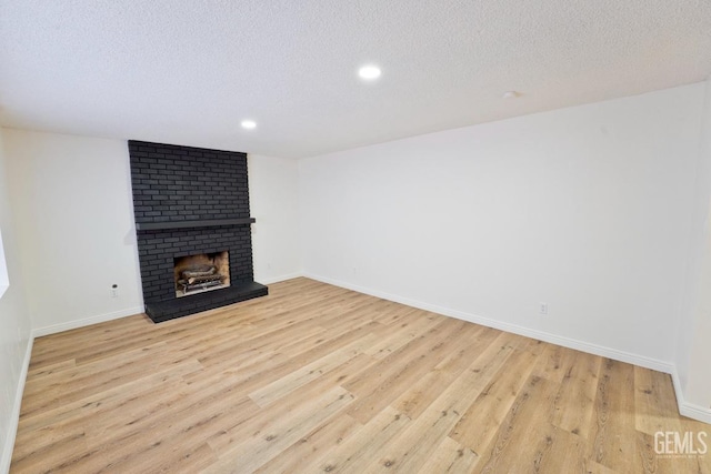 unfurnished living room with light wood finished floors, a fireplace, baseboards, and a textured ceiling