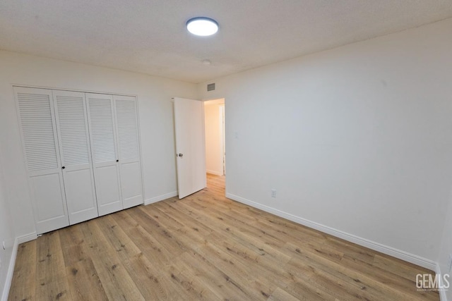 unfurnished bedroom featuring a closet, visible vents, baseboards, and wood finished floors