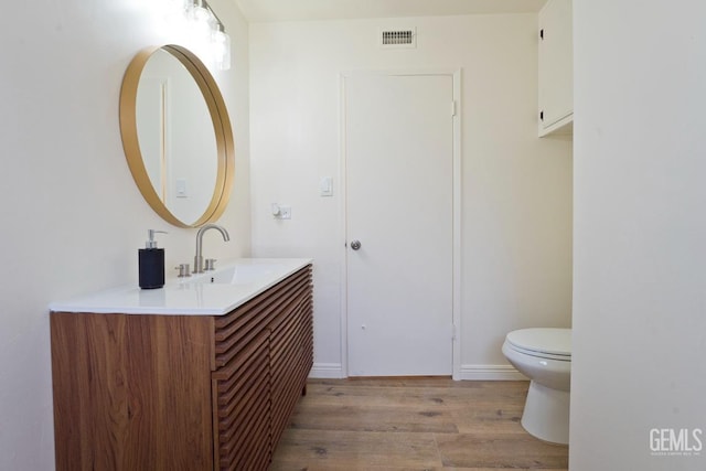 half bathroom featuring toilet, visible vents, wood finished floors, and vanity