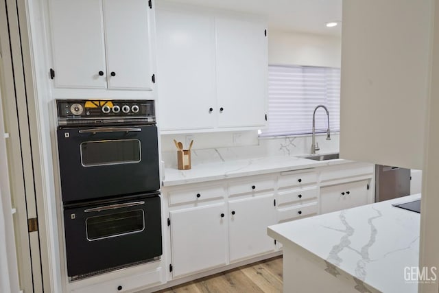 kitchen with light stone counters, white cabinets, dobule oven black, and a sink