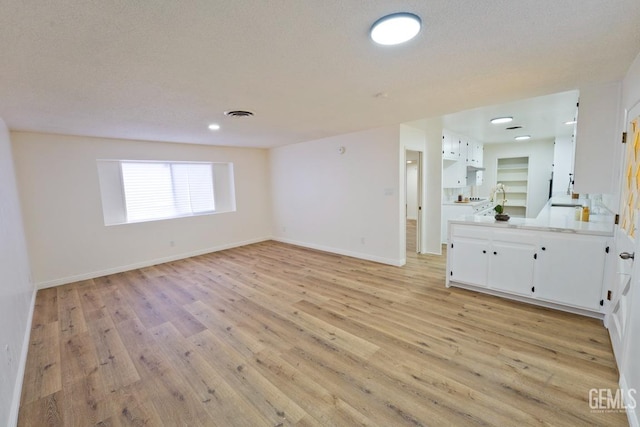 interior space with a textured ceiling, wood finished floors, vanity, visible vents, and baseboards