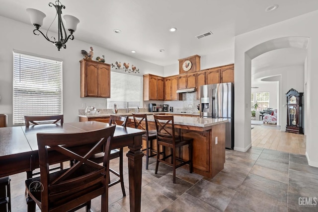 6315 Veronese Ct, Bakersfield, CA 93306 - kitchen with stainless steel fridge, under cabinet range hood, a center island, arched walkways, and brown cabinets