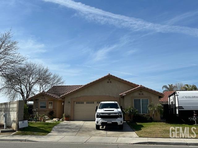 mediterranean / spanish-style home with a garage, concrete driveway, a tile roof, a front lawn, and stucco siding