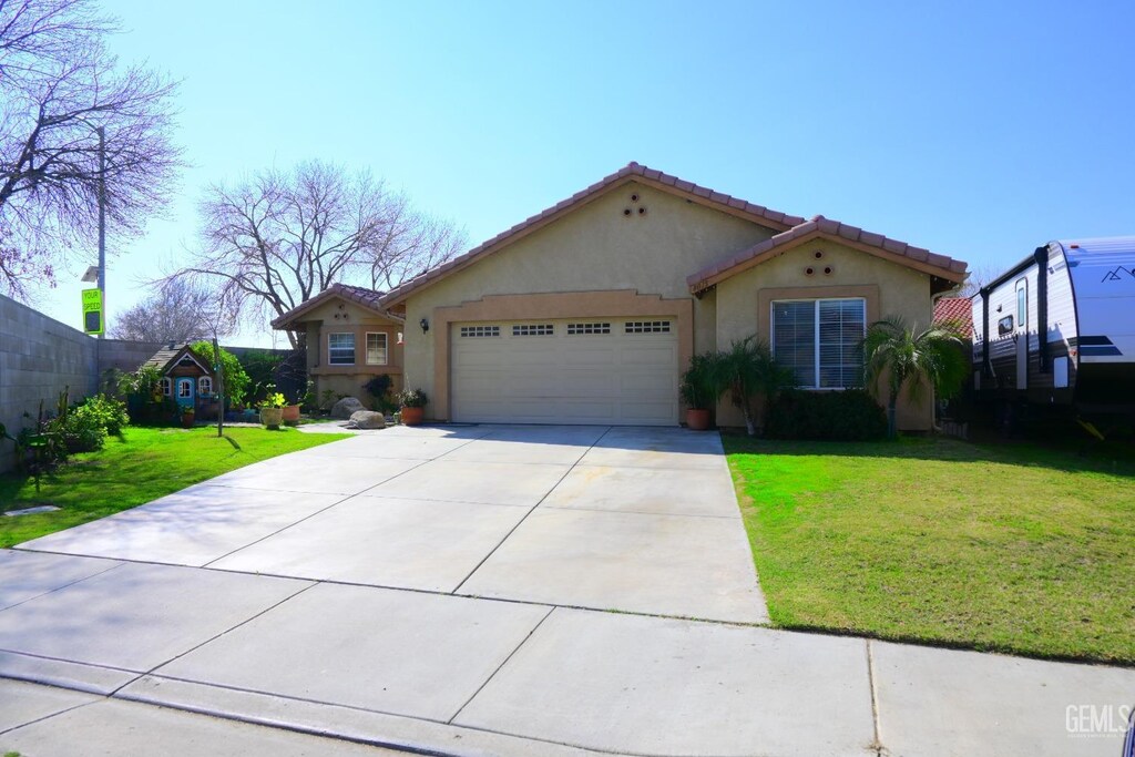 8015 Jackstraw St, Bakersfield, CA 93307 - mediterranean / spanish home featuring a garage, fence, concrete driveway, stucco siding, and a front lawn