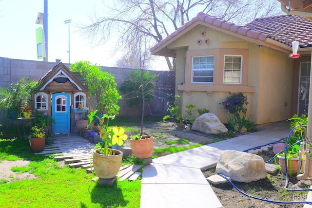 exterior space featuring an outbuilding, fence, a tile roof, and stucco siding