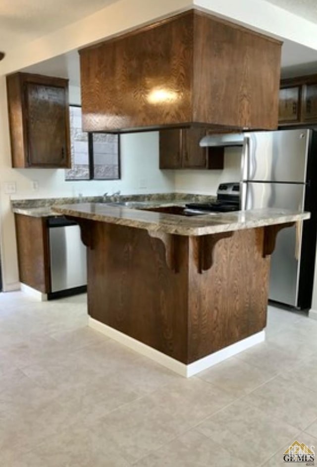 2912 Lum Ave, Bakersfield, CA 93304 - kitchen with stainless steel appliances, exhaust hood, a breakfast bar, a kitchen island, and dark brown cabinets
