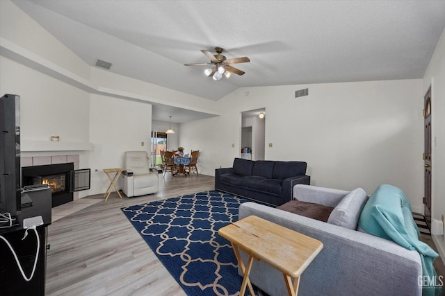 living room with a ceiling fan, visible vents, a tiled fireplace, and vaulted ceiling