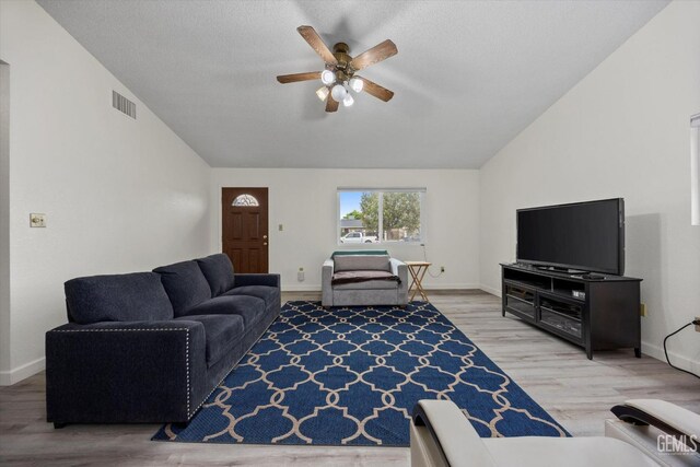 living room featuring a ceiling fan, vaulted ceiling, visible vents, and light wood finished floors