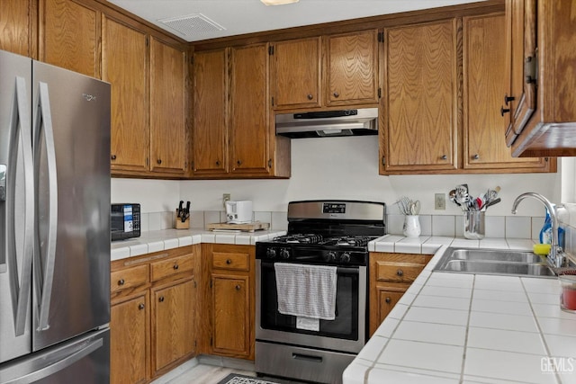 kitchen with visible vents, a sink, under cabinet range hood, tile counters, and stainless steel appliances