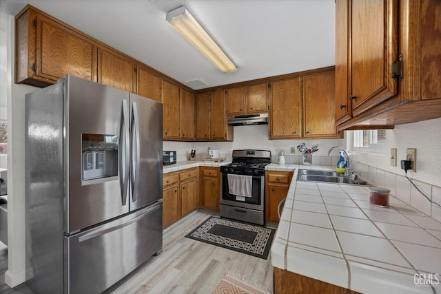 kitchen featuring a sink, brown cabinetry, stainless steel appliances, tile countertops, and under cabinet range hood