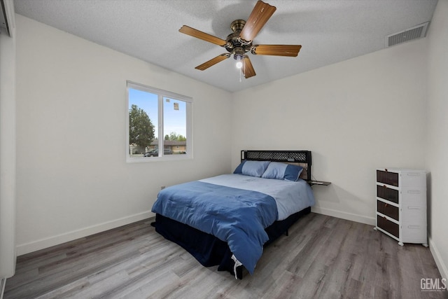 bedroom featuring ceiling fan, baseboards, visible vents, and wood finished floors