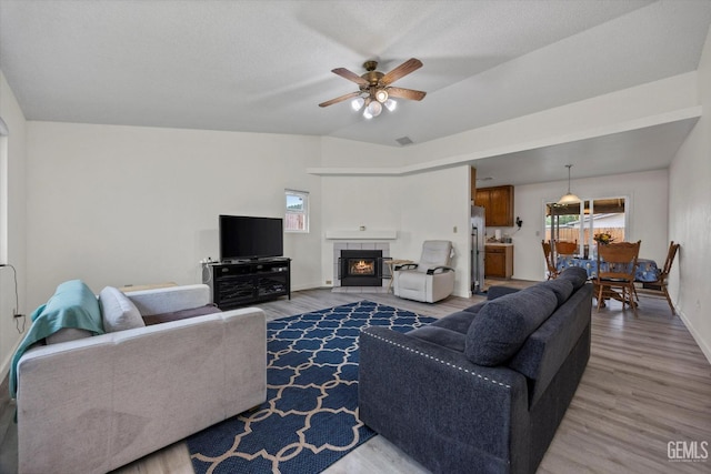 living room with baseboards, ceiling fan, wood finished floors, and a tile fireplace