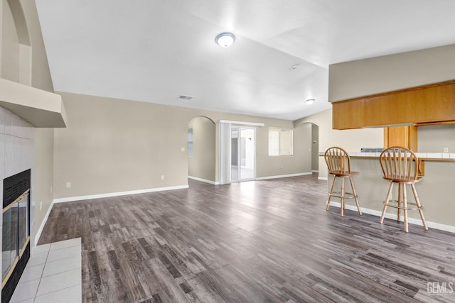 unfurnished living room featuring visible vents, arched walkways, dark wood-type flooring, vaulted ceiling, and a fireplace