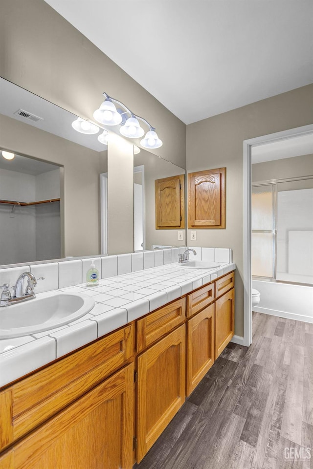 bathroom featuring toilet, wood finished floors, a sink, visible vents, and double vanity