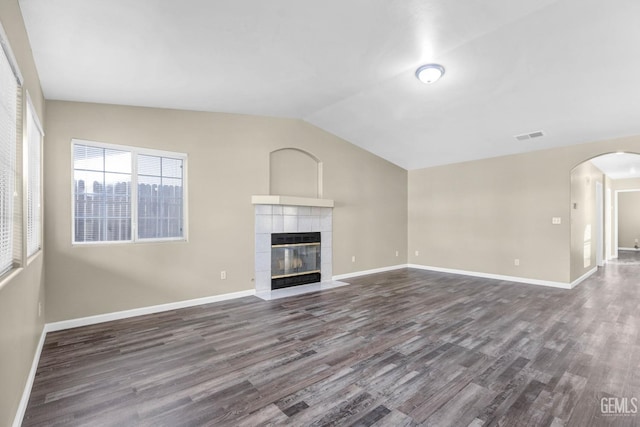 unfurnished living room featuring dark wood-type flooring, lofted ceiling, arched walkways, and a tiled fireplace