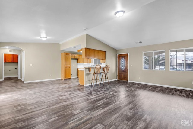 unfurnished living room featuring arched walkways, dark wood-style flooring, visible vents, vaulted ceiling, and baseboards